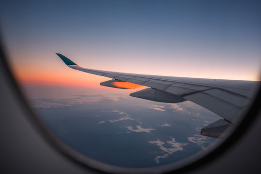 Silhouette wing of an airplane at sunrise view through the window.