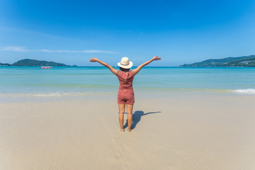 happy travel woman stand on sand of the sea with blue sky at sunny day. subject is blurred.