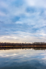 The tranquil water surface on the calm river with the forest strip on the horizon at the morning time