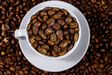 Roasted coffee beans in white cup on coffee beans background. Top view