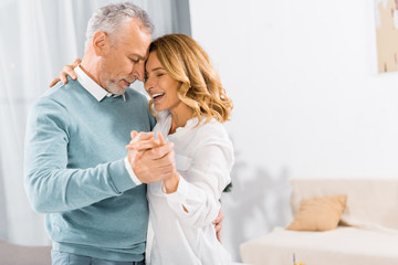 Fototapeta premium side view of happy mature couple dancing face to face at home