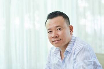 Portrait of Asian mid adult man wearing striped shirt sitting indoor