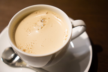 White porcelain cup of milk tea (tea with milk isolated) with teaspoon on a table (a cafe in Jimbocho, Tokyo)