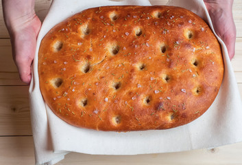 Traditional Italian focaccia homemade bread hold on your hands on a liana napkin. View from the top.