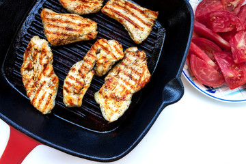 Roasted chicken breast in grill pan, top view. Ripe sliced tomatoes. Isolated on white.