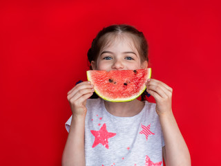 cute little girl holding a watermelon a red background, concept of a healthy diet