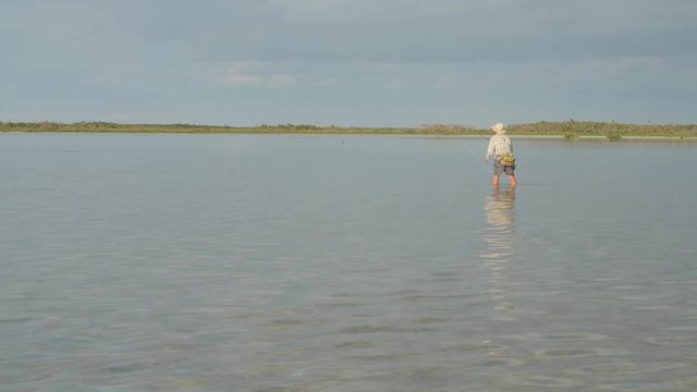 Man wading in a flat lagoon fishing for bonefish