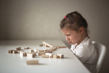 Sad child girl builds of wooden constructor