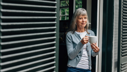 Fototapeta premium Senior woman standing at the door holding a coffee cup