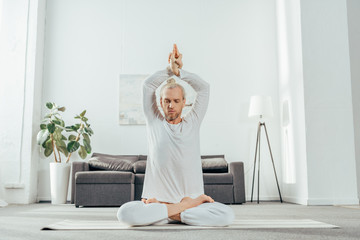 adult man meditating in lotus position with mudra sign on yoga mat at home