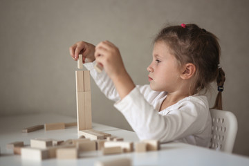 Sad child girl builds of wooden constructor