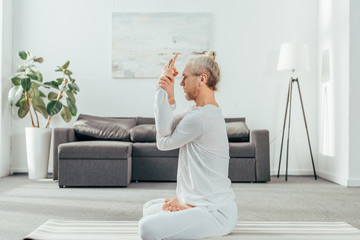 side view of man sitting in lotus position with mudra sign at home