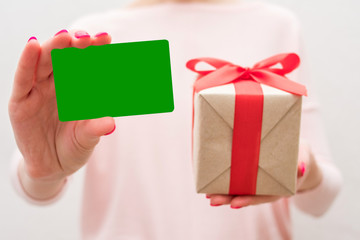 Woman holding a box with a gift, showing business card to the camera, front view, close up, background with copy space, for advertising or slogan
