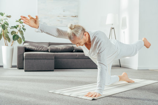 Man Standing In Balancing The Cat Pose On Yoga Mat At Home