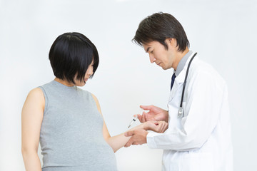 大きなお腹の妊婦が医師から注射をされる様子。