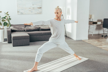 Full length view of man standing in warrior yoga pose on mat at home
