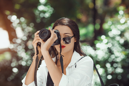 Attractive woman photographer taking images with dslr camera outdoors in park. Gorgeous happy mixed race Asian Caucasian female enjoying traveling outdoors during holidays in Europe.