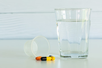 Pills and a glass of drinking water with pill cup isolated on the white table