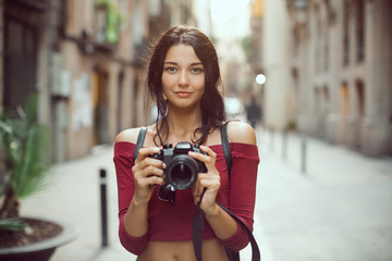 Attractive tourist woman photographer with dslr camera looking at camera outdoor in city street in...