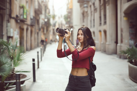 Attractive tourist woman photographer taking images with dslr camera outdoor in city street by digital camera in Barcelona, Spain. Gorgeous happy mixed race Asian Caucasian female in casual hipster