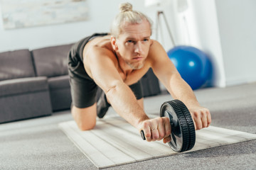 sporty adult man exercising with abs roller at home