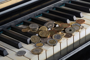 A pile of various coins lying on a piano keyboard