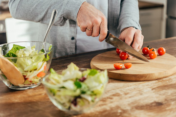 cropped shot of man chopping cherry tomatoes and cooking vegetable salad