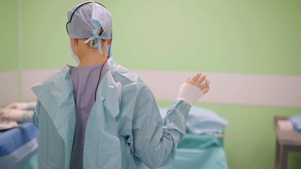 assistants and nurses are helping female surgeon to wear protective and sterile gown before operation
