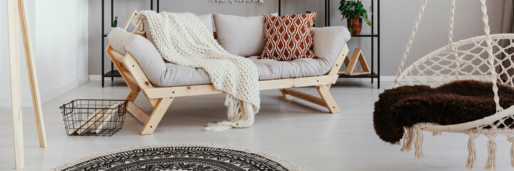 Light grey wooden sofa with knit blanket and patterned cushion in real photo of bright living room...