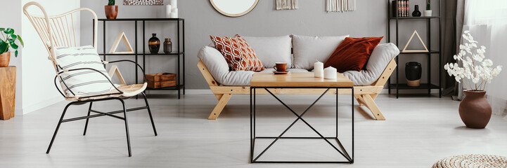 Wood and metal coffee table with candles and tea cup in bright living room interior with grey...