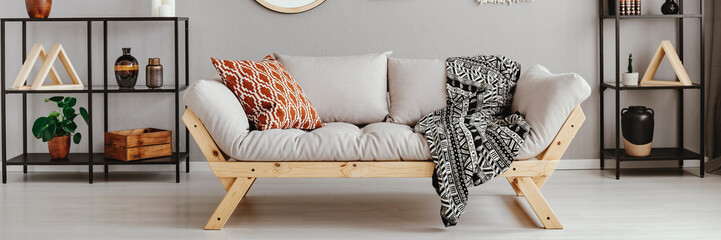 Light grey sofa with patterned pillow and black and white blanket in real photo of scandi living room interior with metal racks with decor - obrazy, fototapety, plakaty