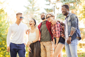 Stylish young people adult men and women using smartphone visit public park during their day off, making a group photo in park. Guys wearing casual clothing and sunglasses.
