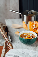 Pumpkin soup with seeds and spicy sauce on the table with fresh sliced pumpkin
