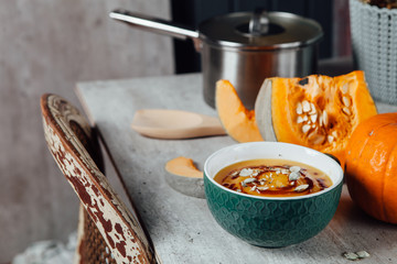 Pumpkin soup with seeds and spicy sauce on the table with fresh sliced pumpkin