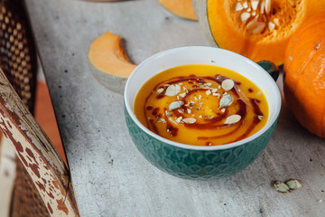 Pumpkin soup with seeds and spicy sauce on the table with fresh sliced pumpkin