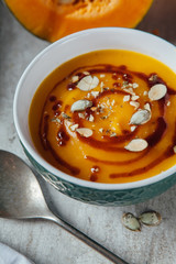 Pumpkin soup with seeds and spicy sauce on the table with fresh sliced pumpkin