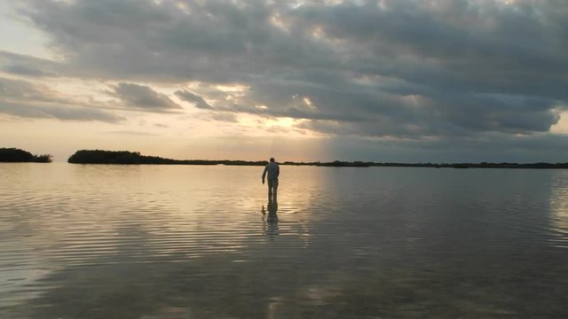 Man wading and fly fishing bonefish in a Lagoon at sunset