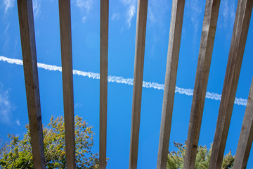 looking up at empty pergola into sky with airplane line
