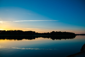 A beautiful and calming sunset accented by a long narrow cloud, a few days after midsummer, reflected on the water of a cove on the Island of Nicklösa in the Åland Islands, Finland.