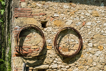 Fototapeta na wymiar Old stone wall with two circles of metal hanging on wall. Green foliage on one side of wall