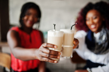 Attractive african american two girls friends sitting at chairs against bar on pub and drinking latte.