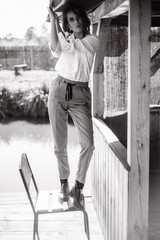 Atmospheric portrait of a beautiful lonely girl walking around a wooden house on the water at the lake