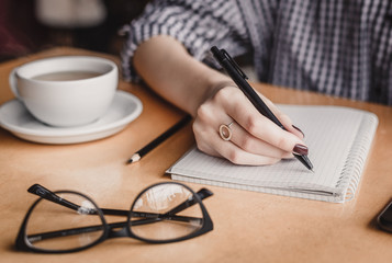 Woman hand writing note pad on wood table in coffee shop