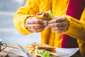 Woman having breakfast in outdoors cafe at city street. Sandwich and coffee on table.