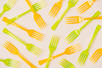 Top view of orange and green plastic forks on pink background