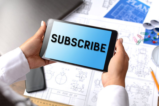 A girl (architect, student, businesswoman) at a table with business accessories, accessories for drawing (plans, rulers) and training with tablet with text Subscribe