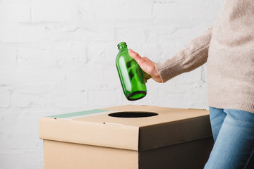 Partial view of woman throwing glass bottle in trash bin