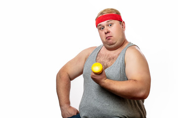 Fat funny man in loose t-shirt and red headband shows his muscles with little yellow dummbell,...