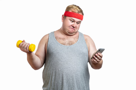 Astonished obese funny man wearing white singlet, looking at smartphone with surprisment while training with dumbbell, being surprised to see that he has lost such a little amount of calories