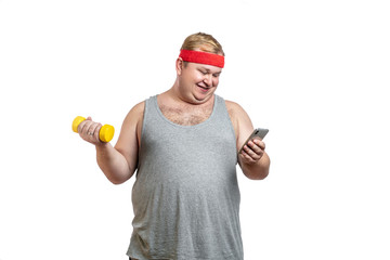 Ironic shot of happy fat man in red hairband exercising with dumbbells and looking at camera isolated on white